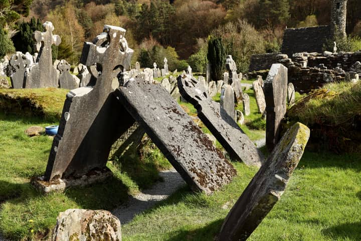 Ancient Celtic gravestones in a green Irish cemetery under a bright sky, showing historical significance.