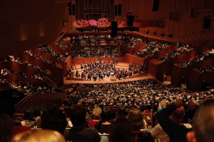 A large audience enjoys a symphony orchestra performance at the iconic Sydney Opera House.