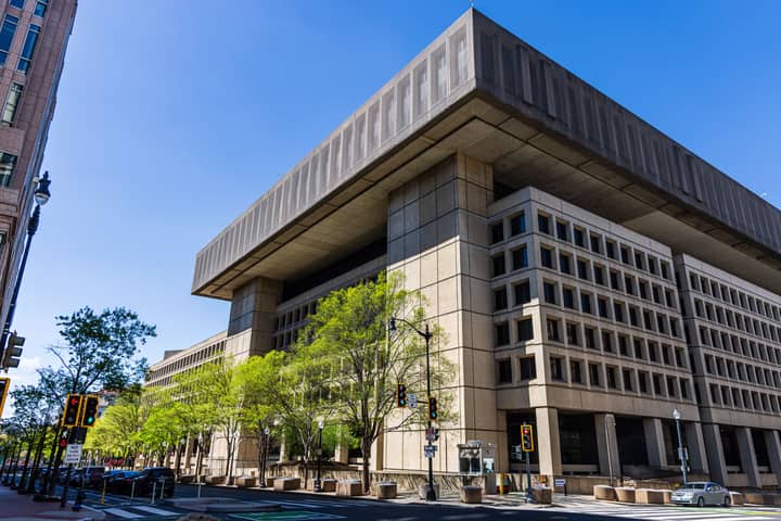 Photo of a modernist government building with a distinct overhang, taken on a sunny day with clear blue skies.