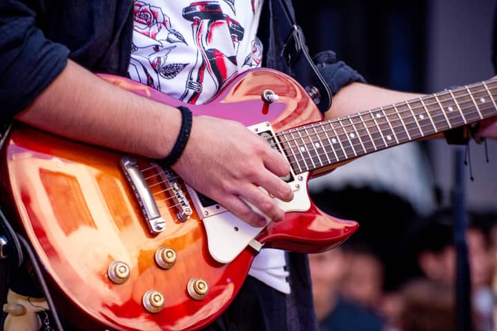 Vibrant close-up of a guitarist performing with a red electric guitar at an outdoor event.