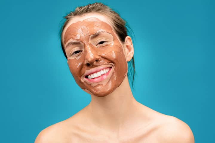 Portrait of a smiling woman with a clay face mask promoting skincare and wellness.