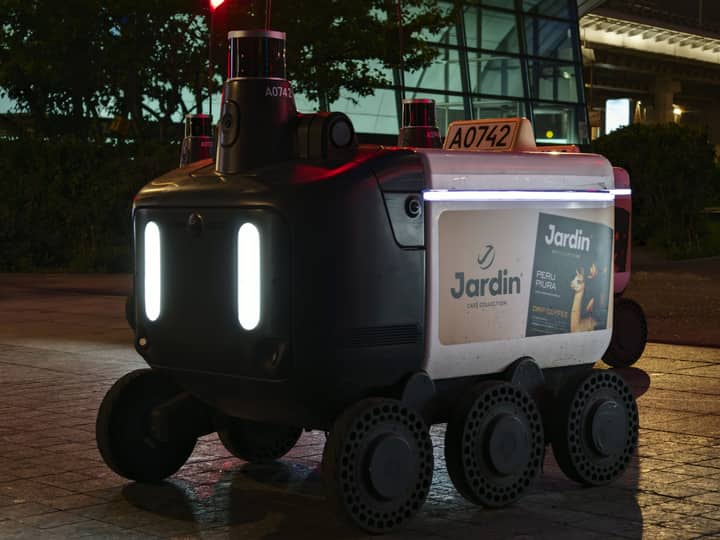 Close-up view of an autonomous delivery robot on a city street at night under artificial light.