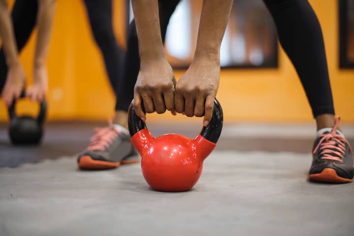 Close-up of hands gripping a red kettlebell in a vibrant indoor gym setting.