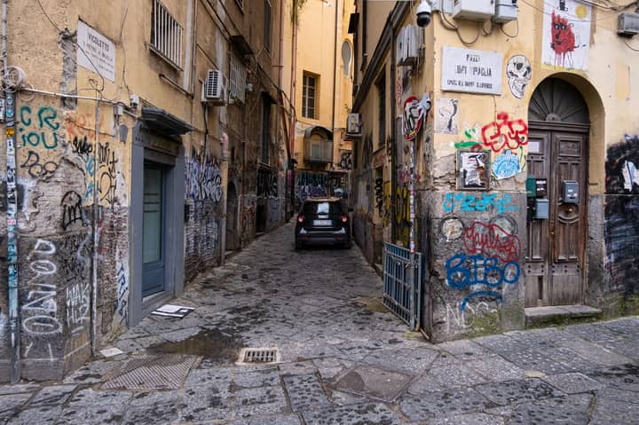 A narrow alley in Naples with colorful graffiti and an old building facade.