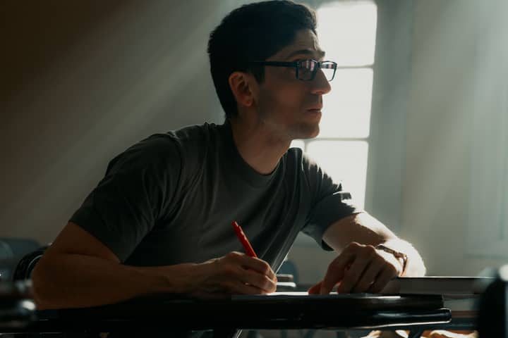 A young adult writing attentively in a classroom illuminated by soft sunlight.