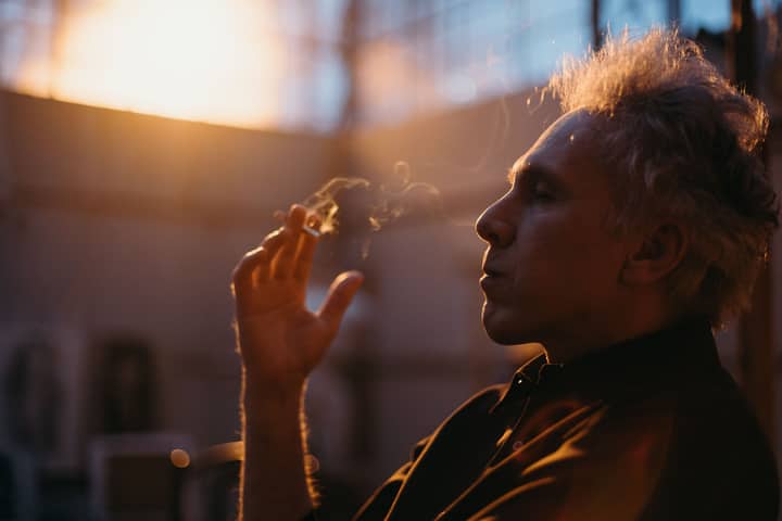 Senior man sitting and smoking indoors, captured with backlit lighting.