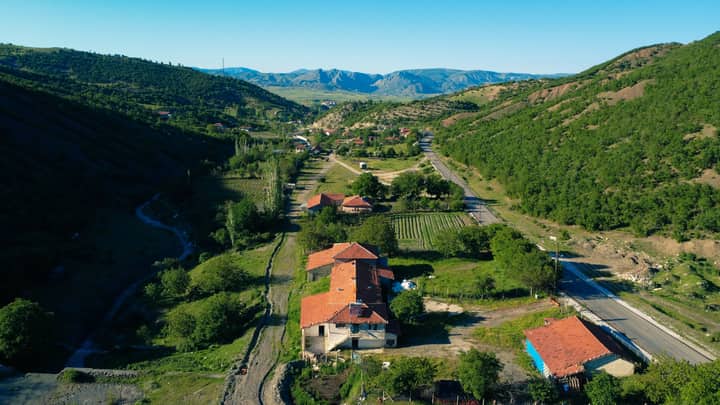 A stunning aerial view of a picturesque village nestled in a lush green valley under a clear blue sky.