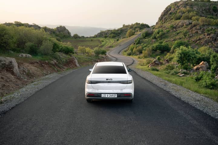 A white car travels down a winding road in the lush hills of Shaqlawa, Iraq, showcasing serene scenery.