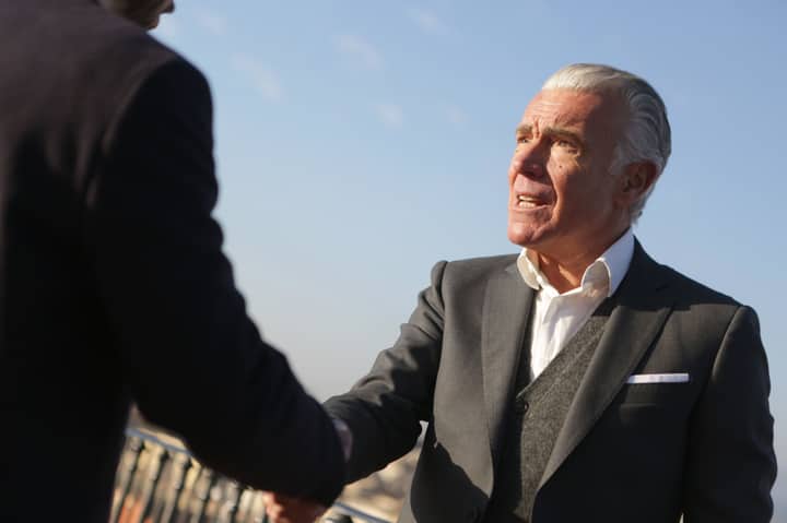 From below of serious male chief director in classy wear standing on street and shaking hands with business partner while reaching agreement and looking at each other