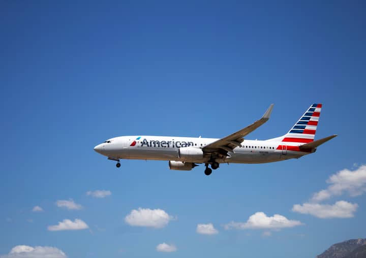 An American Airlines plane flying through a clear blue sky, showcasing aviation travel.
