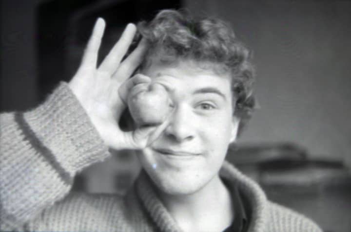 A black and white portrait of a young man playfully holding an object to his eye.