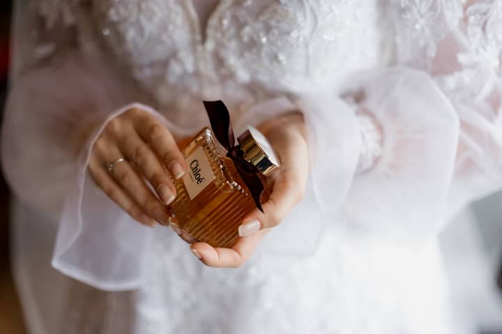 A bride in white lace dress holding a luxury Chloe perfume bottle, symbolizing elegance and style.