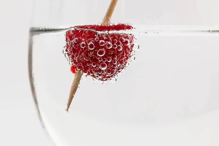 Close-up of a raspberry in sparkling water, highlighting freshness and effervescence.