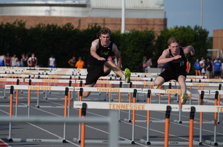 Athletes leap over hurdles in a competitive track event at Tennessee. High energy and focus.