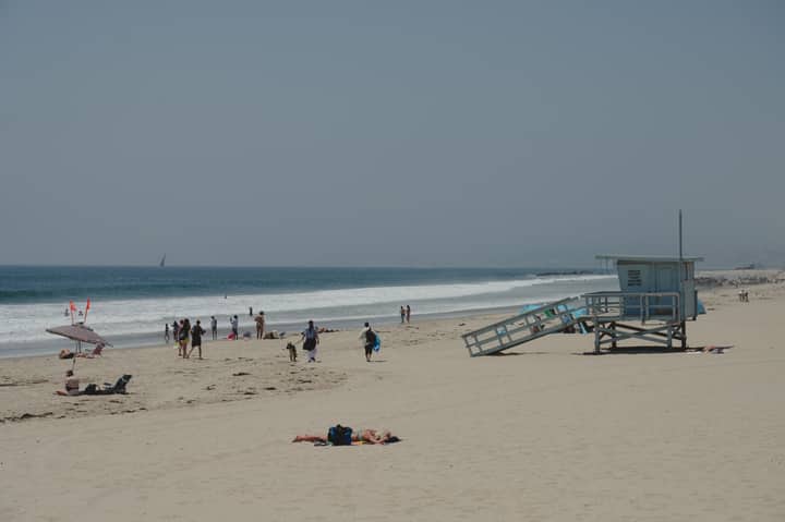 Sunbathers and beachgoers at Santa Monica Beach with iconic lifeguard tower on a sunny summer day.