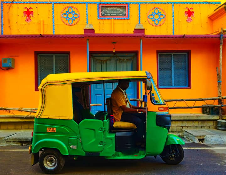 A green and yellow auto rickshaw parked on a colorful Indian street with vibrant architecture.