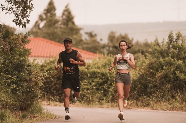 Two athletes jogging on an outdoor trail during a marathon, surrounded by greenery.