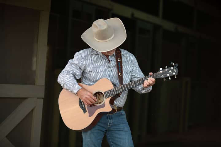 A cowboy in a hat strumming an acoustic guitar, evoking rustic charm and music in a barn.