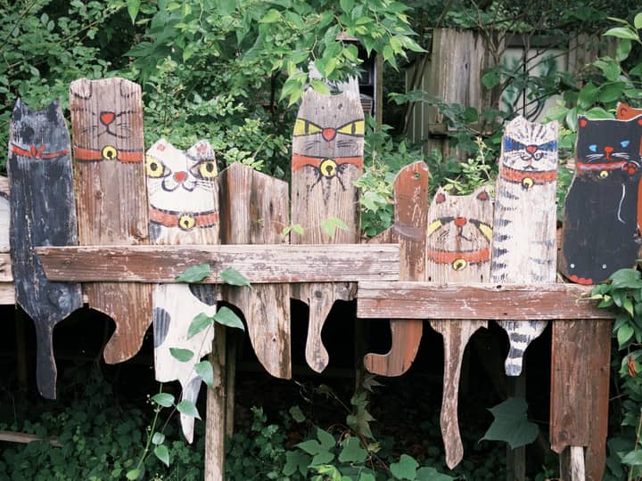 Charming wooden cat decorations on a rustic fence surrounded by lush greenery.