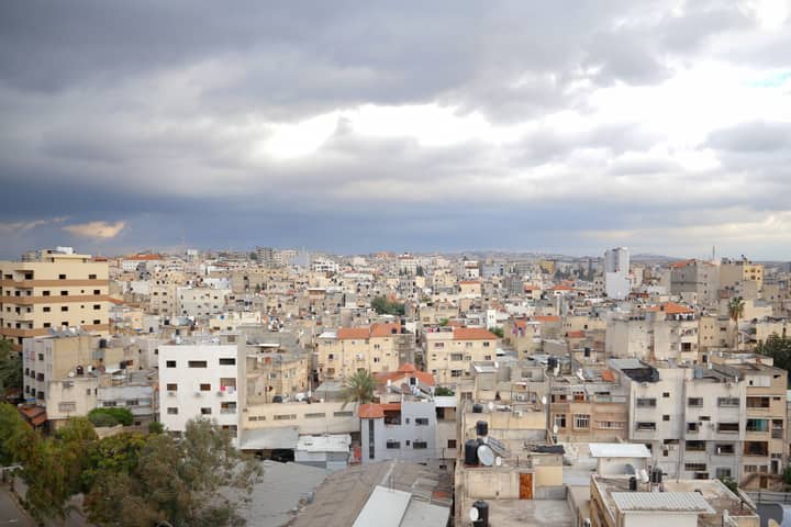Aerial view of Qalqilya's urban cityscape under dramatic clouds, showcasing diverse architecture.