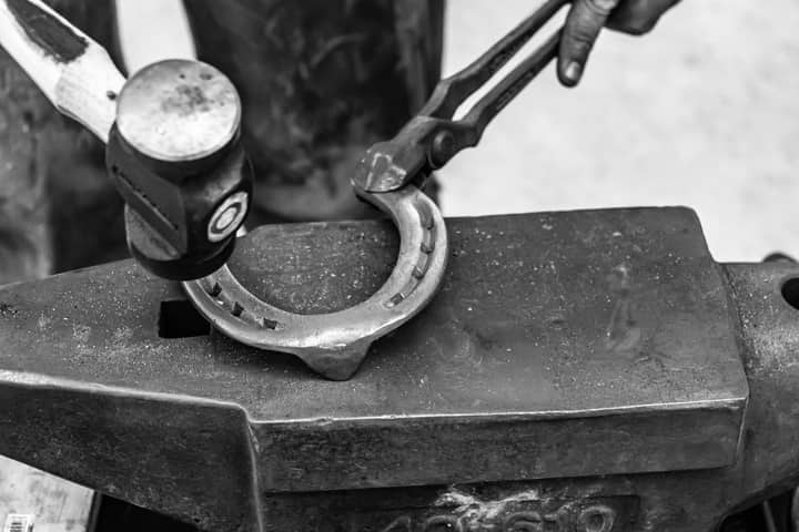 Black and white image of a blacksmith shaping a horseshoe with a hammer on an anvil.
