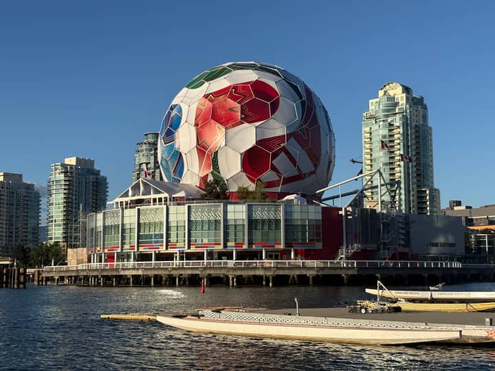 A massive soccer ball decorates Science World, set against Vancouver's iconic skyline and waterscape.