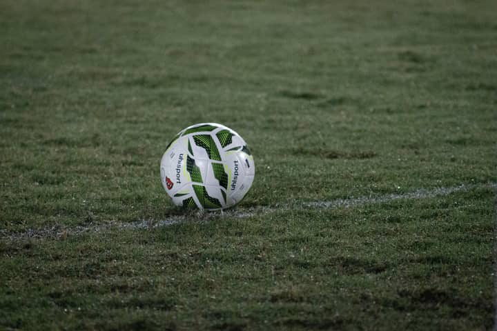 A soccer ball resting on a grass field, captured during nightfall with visible dew.