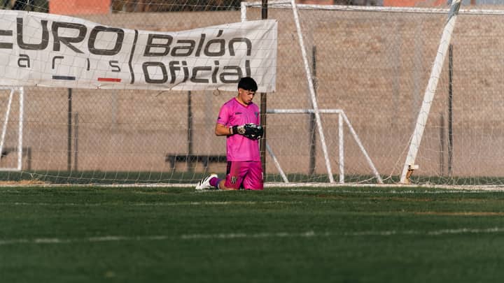 Young soccer goalkeeper in pink gear kneeling on the field during practice.