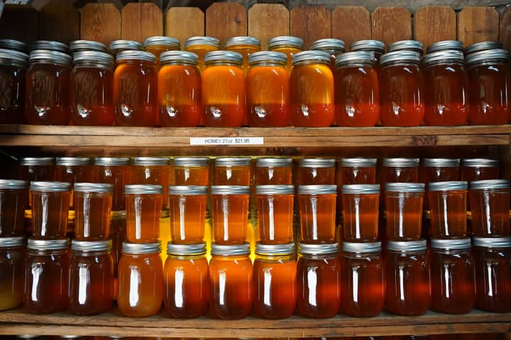 Dozens of honey jars on shelves in a rustic setting create a warm, inviting display.