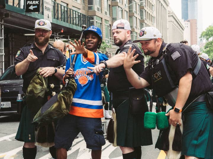 Group of bagpipers and a fan posing at a street parade with joyful expressions.