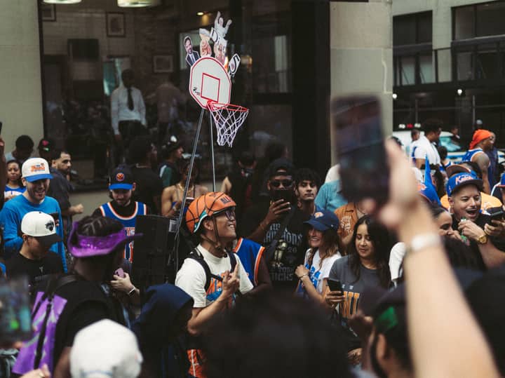 Vibrant street scene of basketball fans wearing jerseys and celebrating with a mini hoop setup.