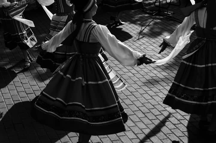 Black and white image of traditional folk dancers in elegant dresses performing outdoors.