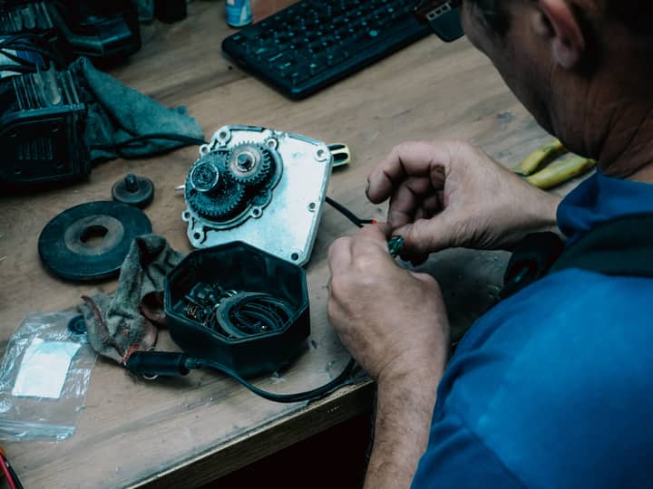 An adult male technician repairing a mechanical gear system on a wooden table indoors.