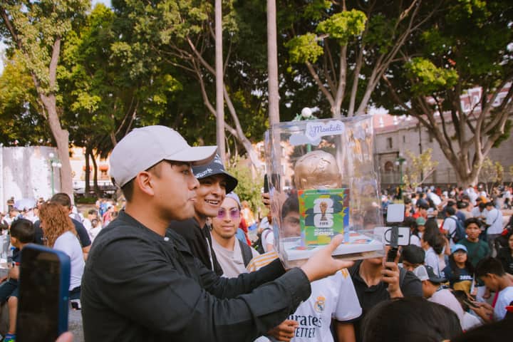 Group of people celebrating with a FIFA World Cup trophy replica in a vibrant outdoor setting.