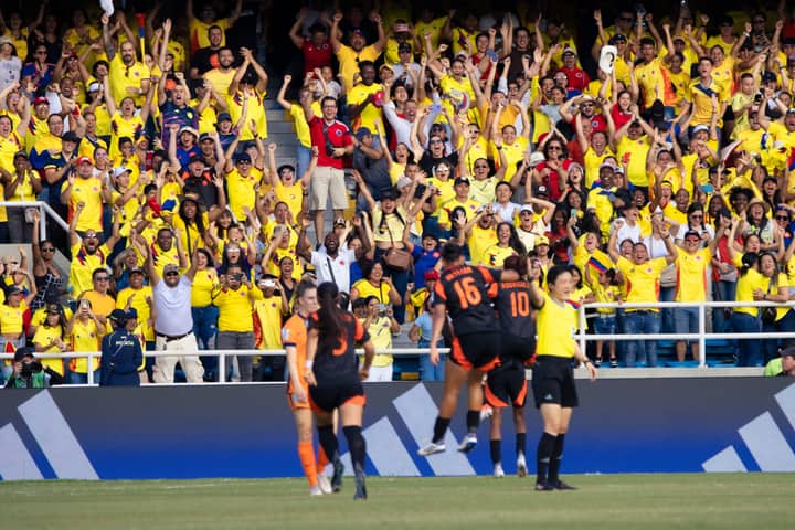 Energetic crowd of Colombian football fans cheering at a match in a vibrant stadium.