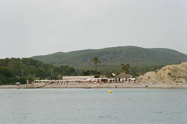 Serene beach scene in Eivissa with lush green hills and a distant resort.