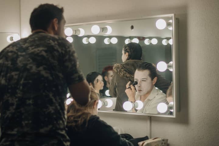 Actors applying makeup backstage in illuminated dressing room before a performance.