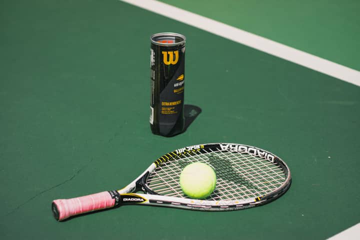 Tennis racket and ball on a bright green court next to a tube of balls.