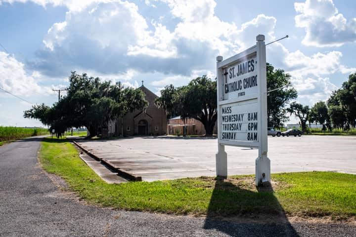 St. James Catholic Church with signage in a rural setting, captured under a bright sunny sky.