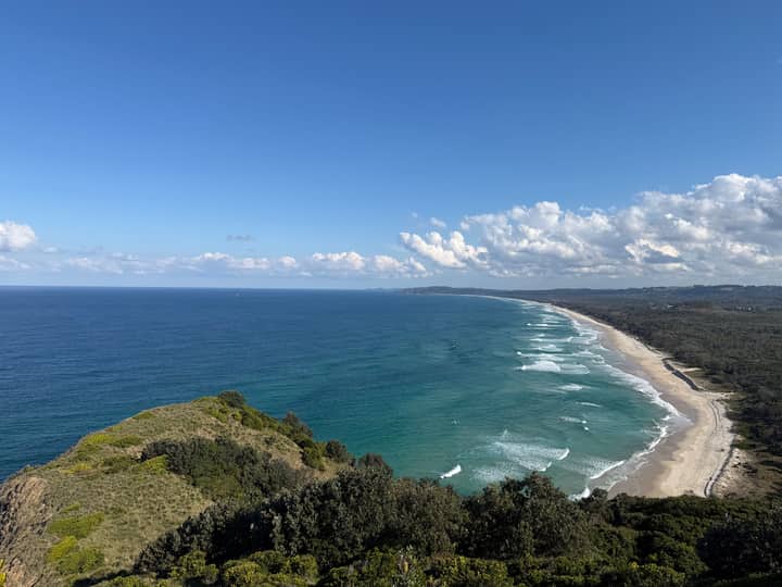 Stunning aerial photo of Byron Bay coastline with lush greenery and expansive ocean under a clear blue sky.