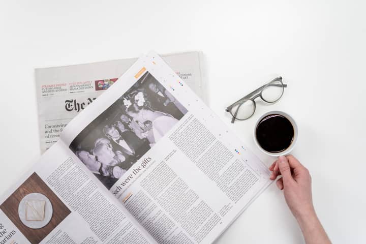 Overhead view of newspaper reading with coffee and glasses on a white table.