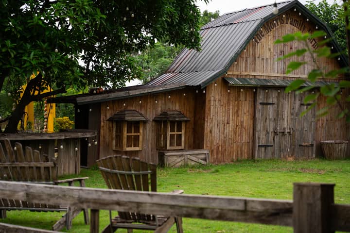 An inviting rustic wooden barn surrounded by lush greenery and cozy outdoor seating, perfect for a peaceful retreat.