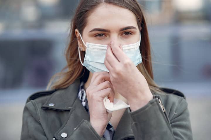 Portrait of a young woman adjusting her protective face mask while outdoors, focusing on safety and health.