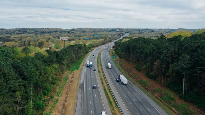 Aerial view of wavy asphalt roads with driving cars and trucks between bright trees under endless cloudy sky in rural zone