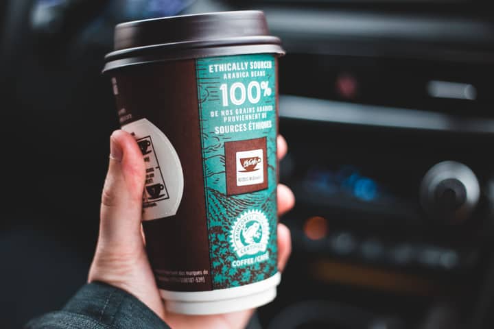 Closeup of faceless guy with disposable cup of hot coffee to go in hand sitting in car