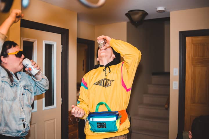 Two friends having a fun indoor party, wearing yellow hoodie and denim, drinking and celebrating.