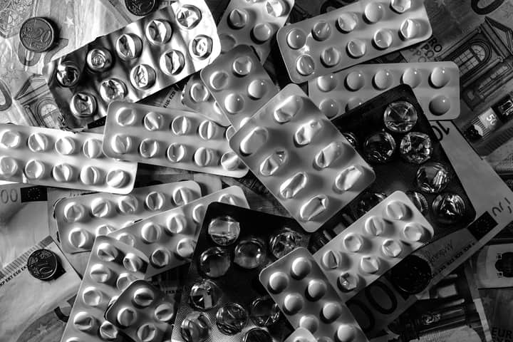 Black and white image of pill blister packs scattered on euro bills and coins.