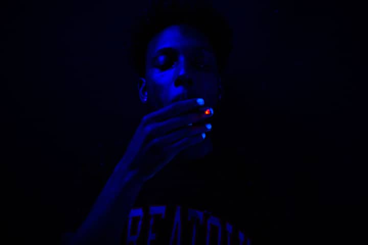 Close-up of a man smoking under blue ultraviolet lighting, creating a dramatic effect.