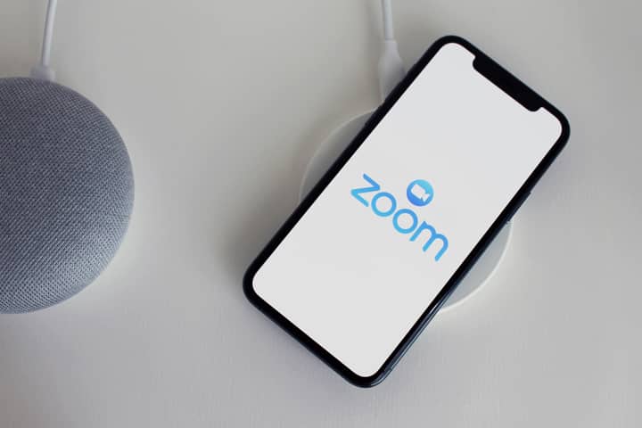 Close-up of a smartphone with Zoom app on a wireless charger next to a smart speaker.
