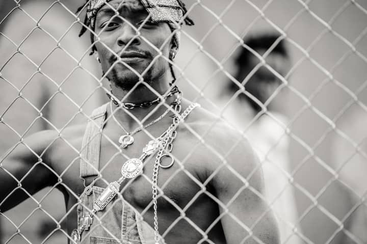 Black and white handsome sporty African American man with beard looking at camera through metallic chain link fence